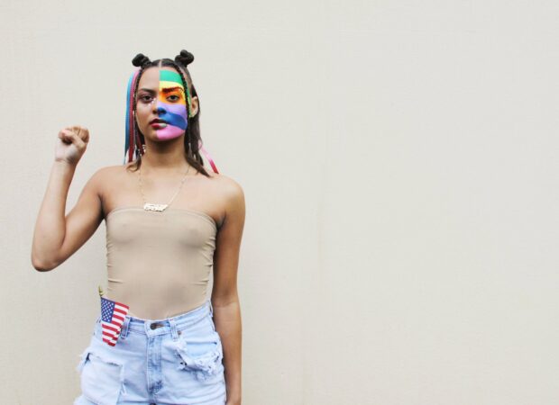 Persona con pintura de la cara de la bandera del orgullo sosteniendo el puño para el movimiento Black Lives Matter