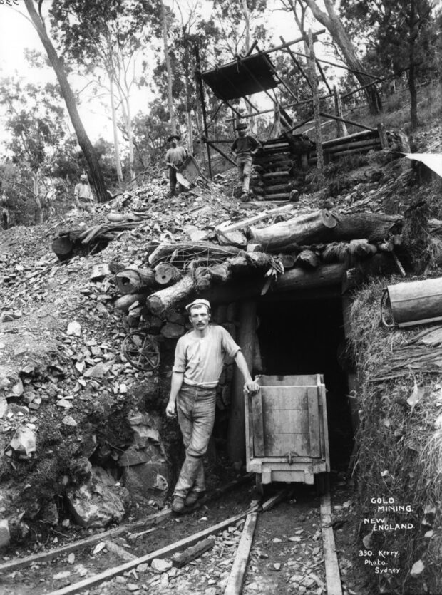 Imagen histórica en blanco y negro del hombre de pie frente a una mina de oro de Nueva Inglaterra