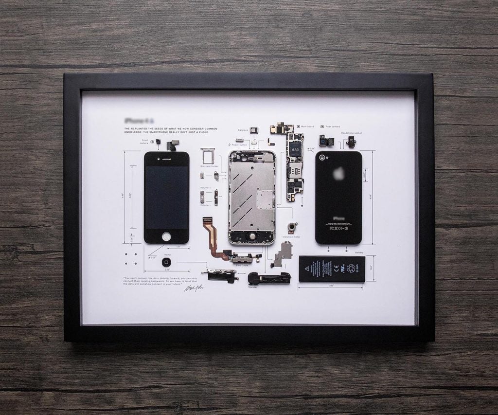 Un marco de fotos sobre un fondo de madera con una foto muestra el iPhone 4s completamente abierto y cada unidad colocada por separado con cada parte etiquetada sobre un fondo blanco.