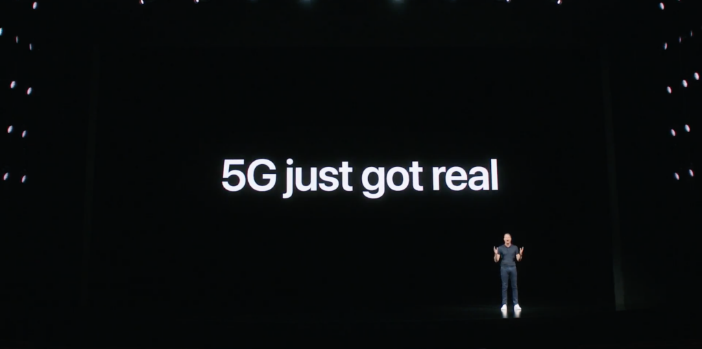 Un tipo parado en un escenario negro con 5G se muestra real en una pantalla detrás