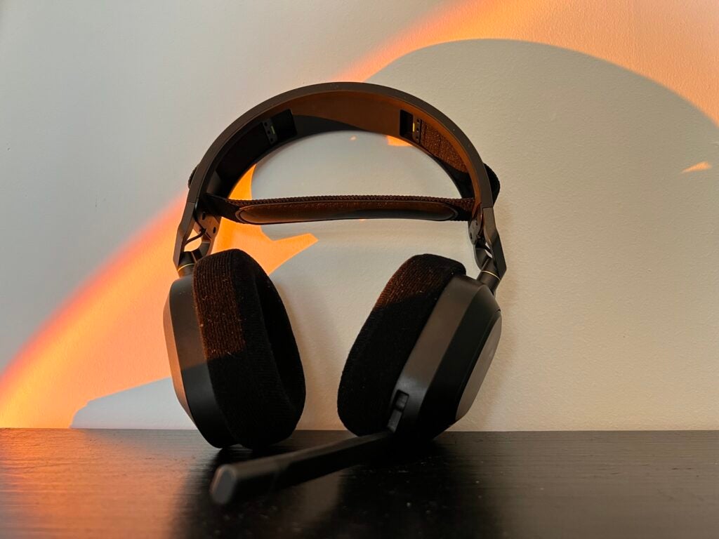 Los auriculares Corsair HS80 RGB apoyados contra una pared sobre un escritorio negro