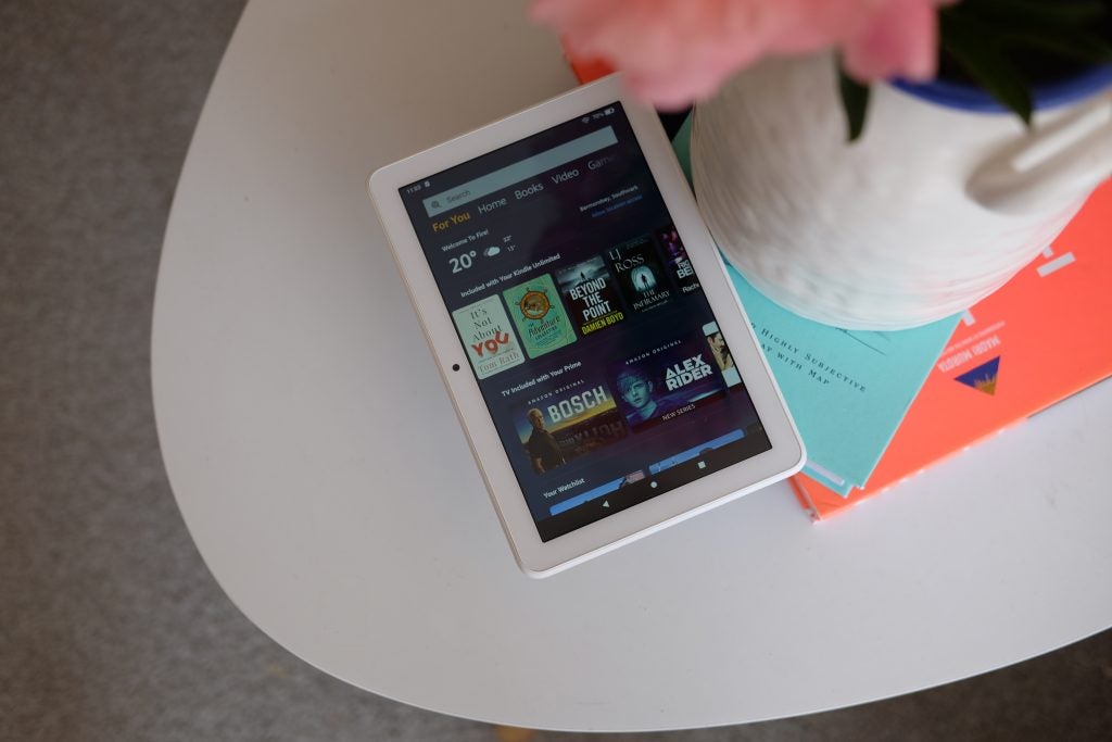 Vista desde la parte superior de un Amazon Kindle blanco colocado sobre libros que muestran la pantalla de inicio de una tienda
