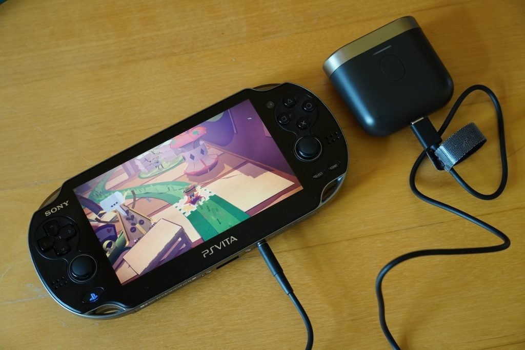 Una playstation PS Vita negra de Sony que muestra un juego con controles de juego en cada lado, un conector conectado y el otro extremo conectado a un altavoz, que muestra la transmisión de audio Bowers and Wilkins P17