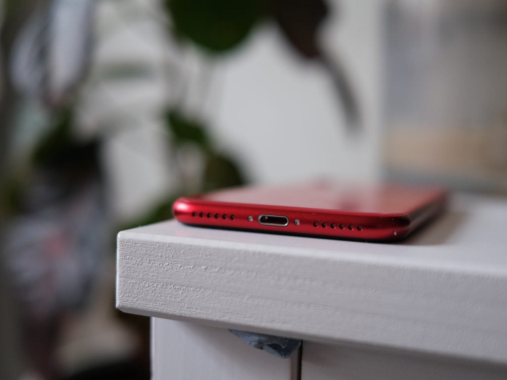 Vista del borde inferior de un iPhone SE rojo colocado boca abajo sobre un estante blanco
