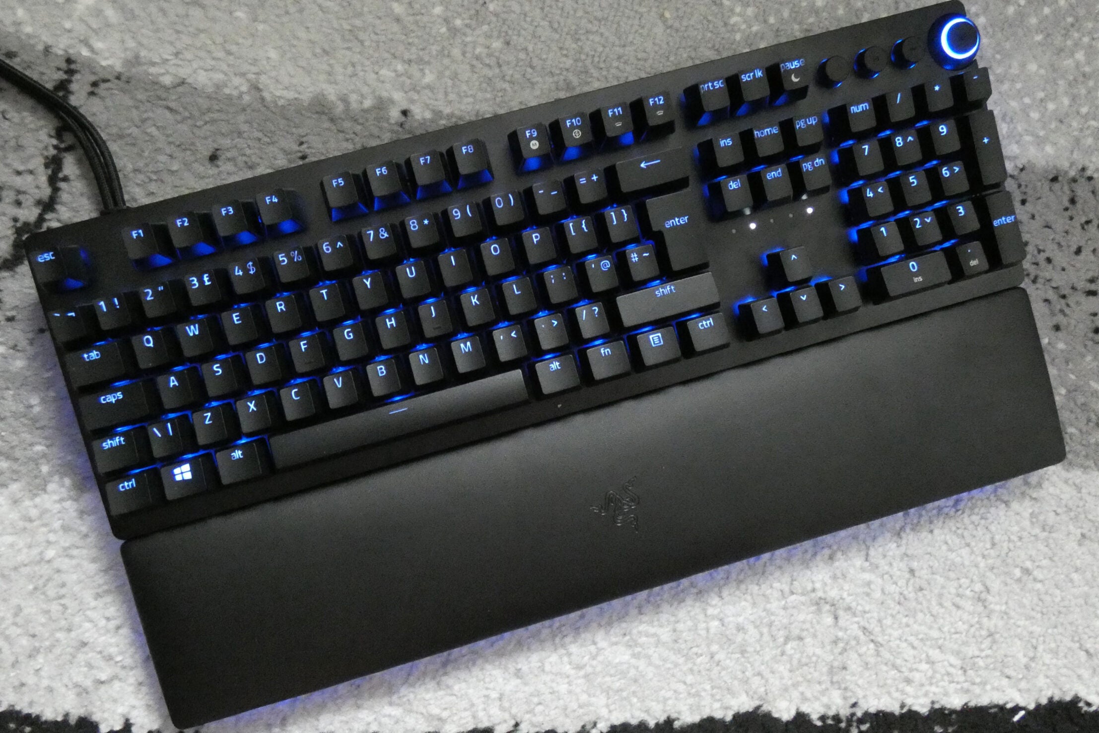 Vista desde arriba de un teclado analógico Huntsman V2 negro con luces azules debajo de las teclas