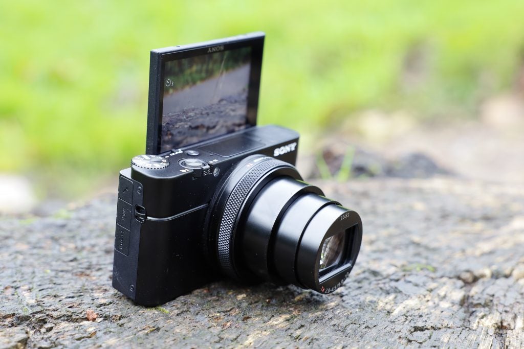 Vista en ángulo izquierdo de una cámara Sony RX100 VII negra parada en el suelo con la pantalla trasera volteada hacia el frente