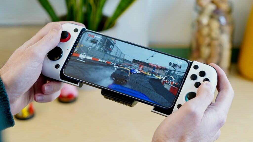 Manos sosteniendo el controlador GameSir X3 conectado al teléfono inteligente con juego de carreras.